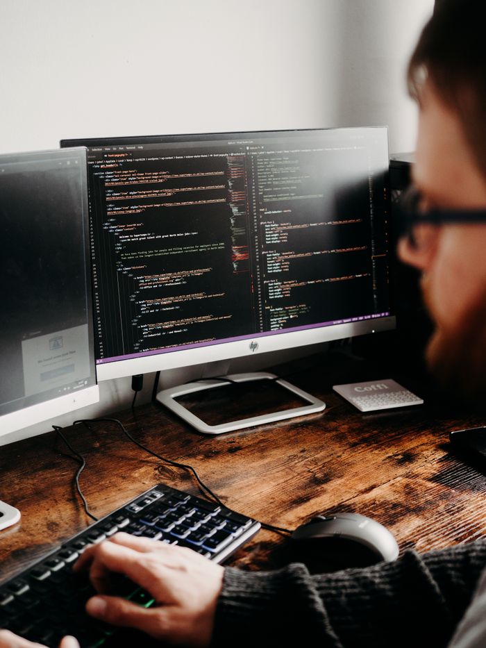 About Focused software developer at desk coding with multiple monitors in a modern workspace.